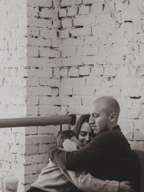 Free Grayscale photo of a couple embracing lovingly by a white brick wall, symbolizing romance. Stock Photo