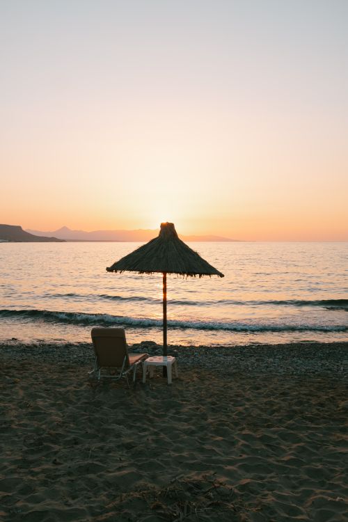 Free Peaceful sunset view with a straw umbrella on a Greek beach. Stock Photo