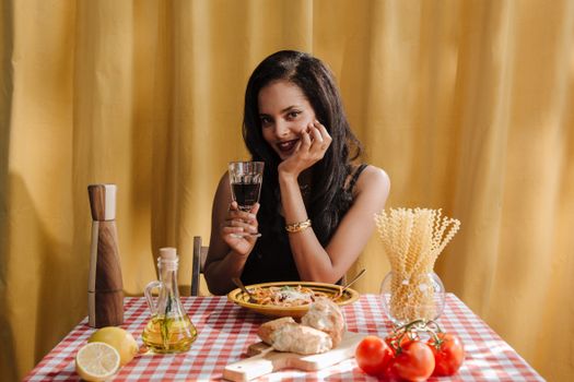 Cheerful woman savoring pasta and wine at a cozy table with vibrant decor.