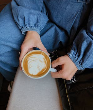 Close-up of hands holding a latte with beautiful latte art in a cozy setting.