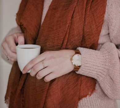 Close-up of a woman holding a cup in cozy knitwear, exuding warmth.
