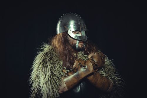 Free Portrait of a Viking warrior wearing a metal helmet and fur cloak, captured against a dark background. Stock Photo