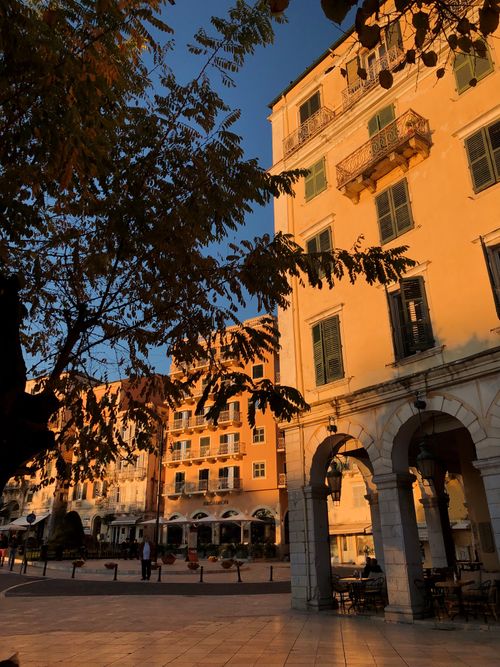 Free Golden hour light on European buildings with arches and trees in a tranquil town square. Stock Photo