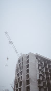 High-rise building under construction with crane on a foggy day.