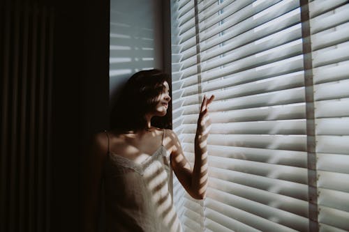 Photo of a Woman Looking Out Window Shutters