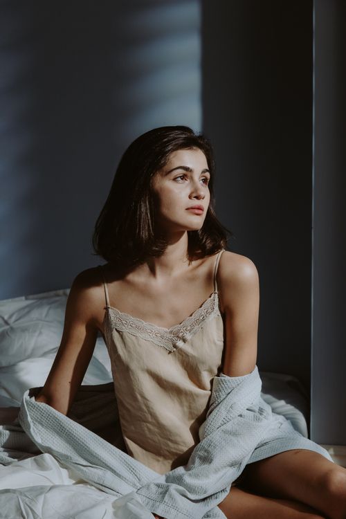 Free A woman in sleepwear poses elegantly in a sunlit bedroom, looking contemplatively to the side. Stock Photo