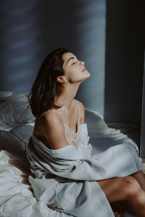 Free A serene moment of a woman sitting in a sunlit bedroom, embracing morning tranquility. Stock Photo