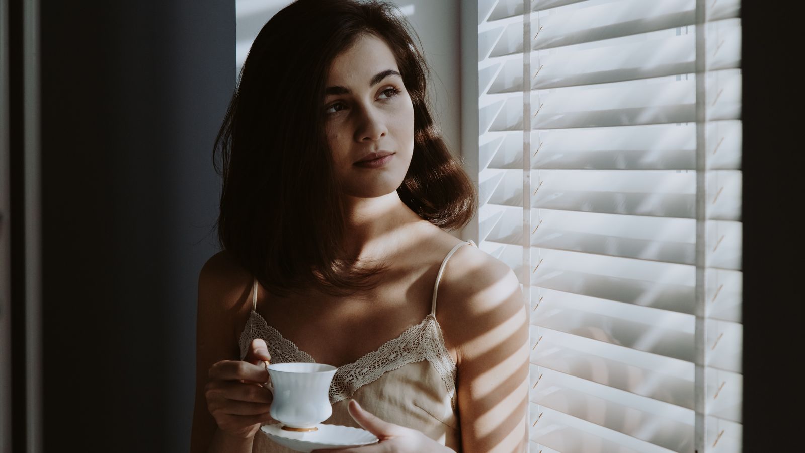 A woman holding a cup of coffee beside a sunlit window