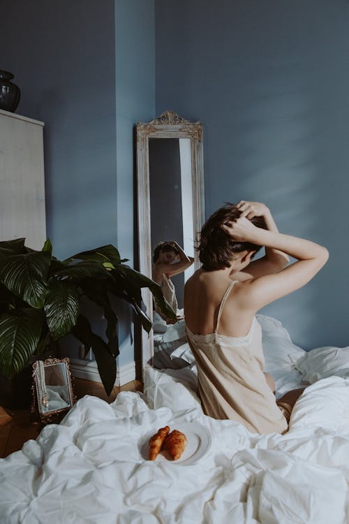 Free A Woman in Nightwear Sitting on Her Bed while Looking at the Mirror Stock Photo