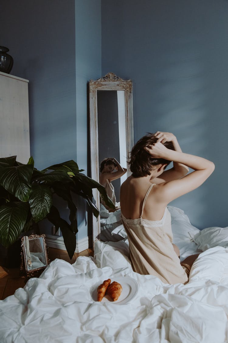 A Woman In Nightwear Sitting On Her Bed While Looking At The Mirror