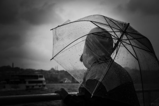 Silhouette of a person with transparent umbrella on a rainy day, overlooking a city waterfront.