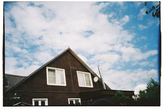 Sunlit wooden house exterior with clear blue sky and fluffy clouds.