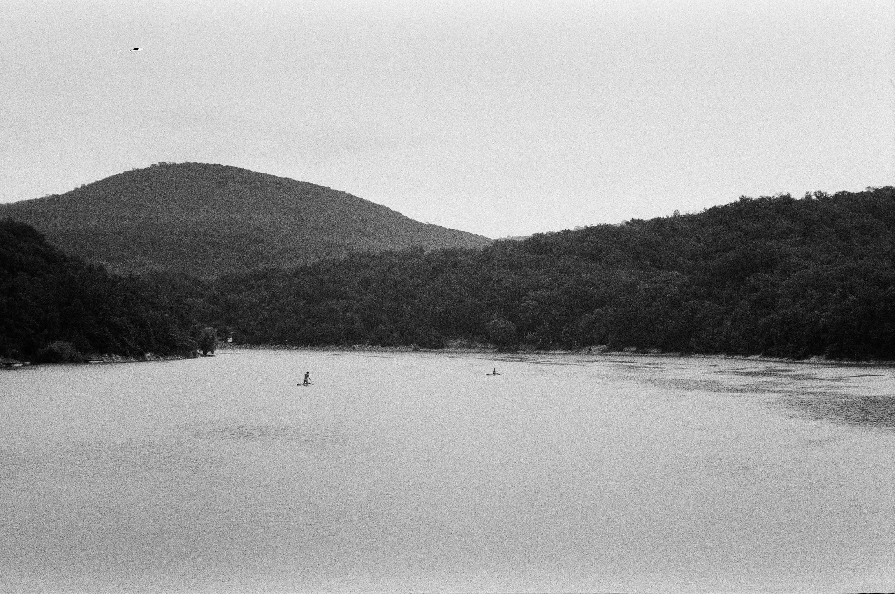 Peaceful black and white photo of a lake surrounded by forested hills.
