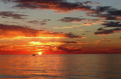 Free A breathtaking sunset over the sea with a silhouette of a boat on the horizon, capturing vivid orange hues. Stock Photo