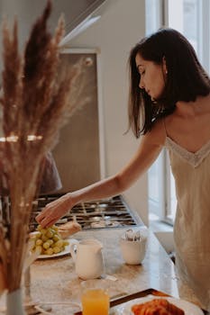 Young woman reaching for grapes in a warmly lit kitchen during breakfast time.