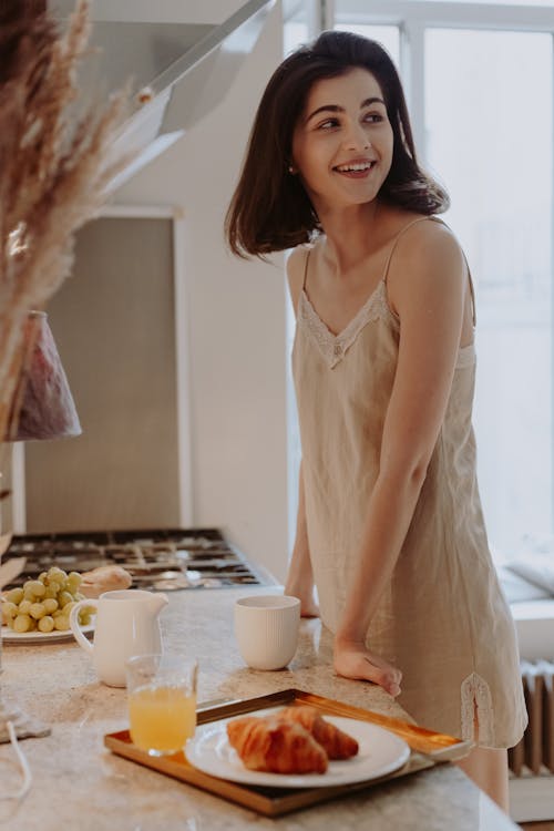 Free Smiling Woman in Nightdress Standing Beside Table With Juice and Croissants Stock Photo