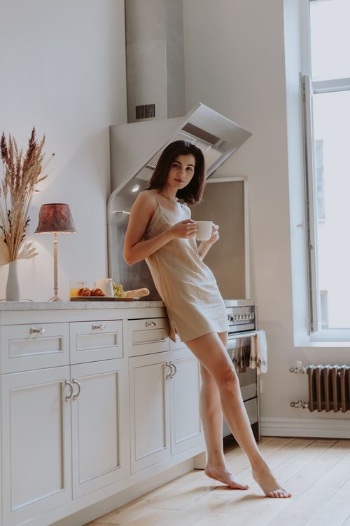 Free A young adult woman enjoys a morning coffee in a cozy, sunlit kitchen with modern decor. Stock Photo