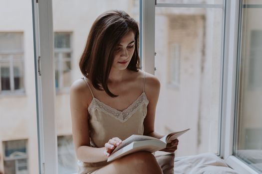 A woman in casual wear reading a book by a window, enjoying a peaceful moment.. woman, casual, wear