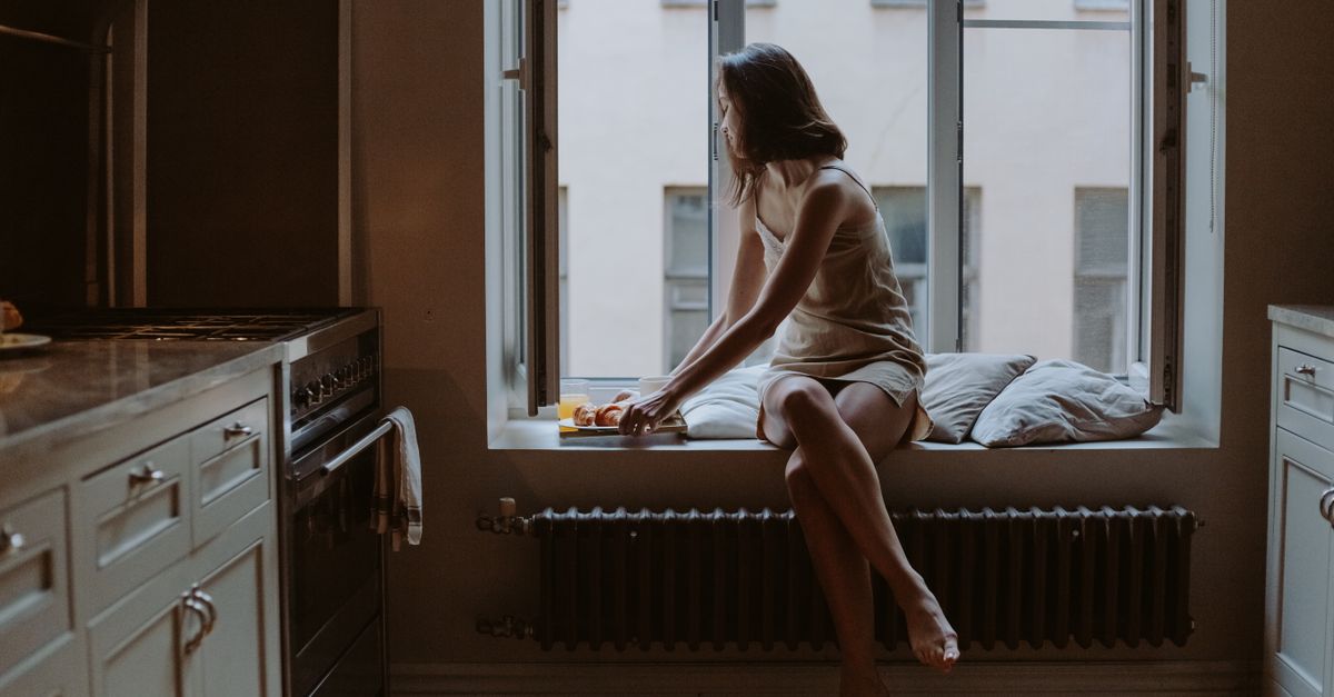 A serene scene of a woman sitting by the window in a cozy kitchen, enjoying a calm moment.