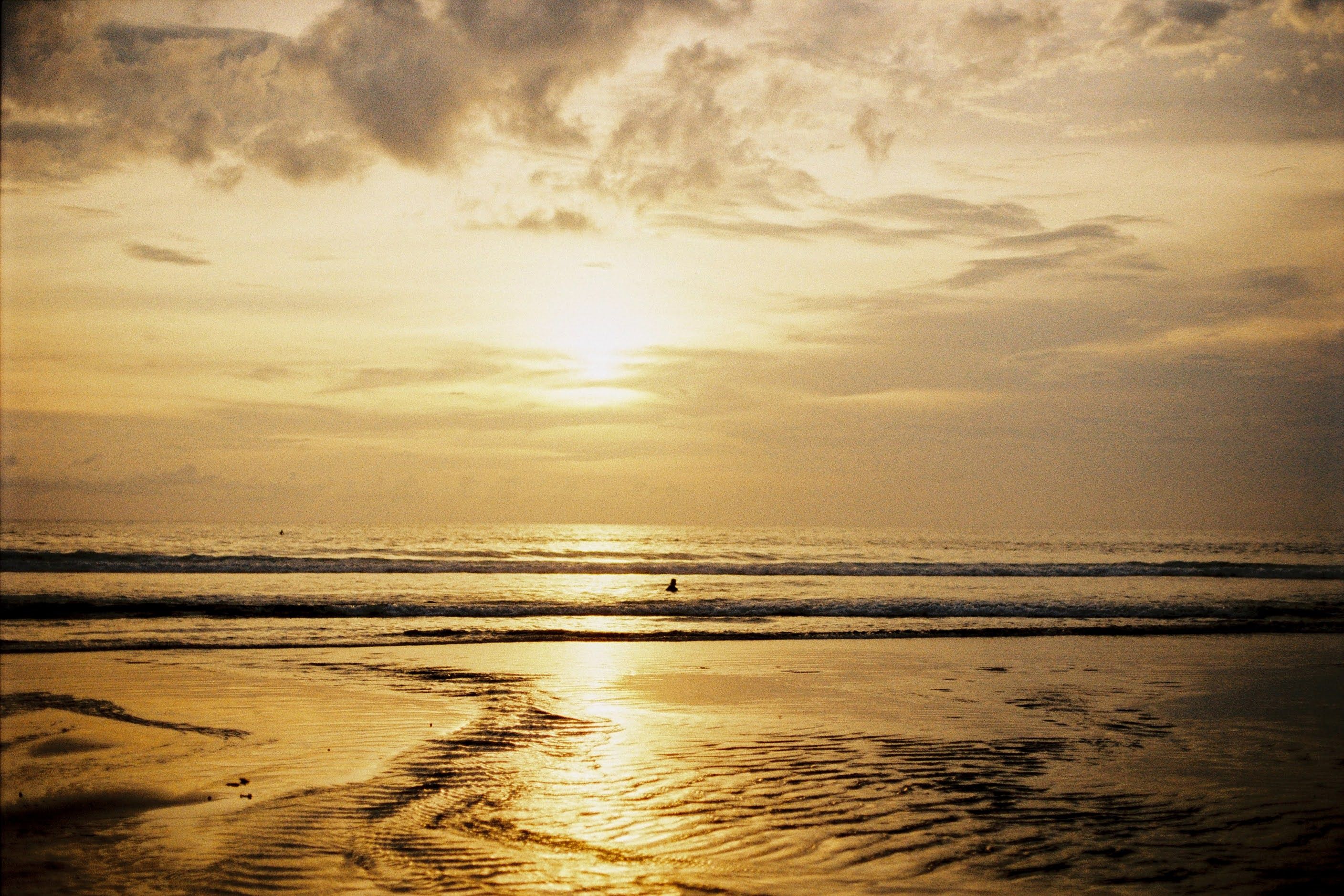 Experience a serene golden hour at a Bali beach with tranquil waves and expansive skies.