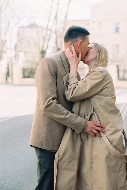 Photo of a Man in a Brown Blazer Kissing a Woman Wearing a Brown Coat