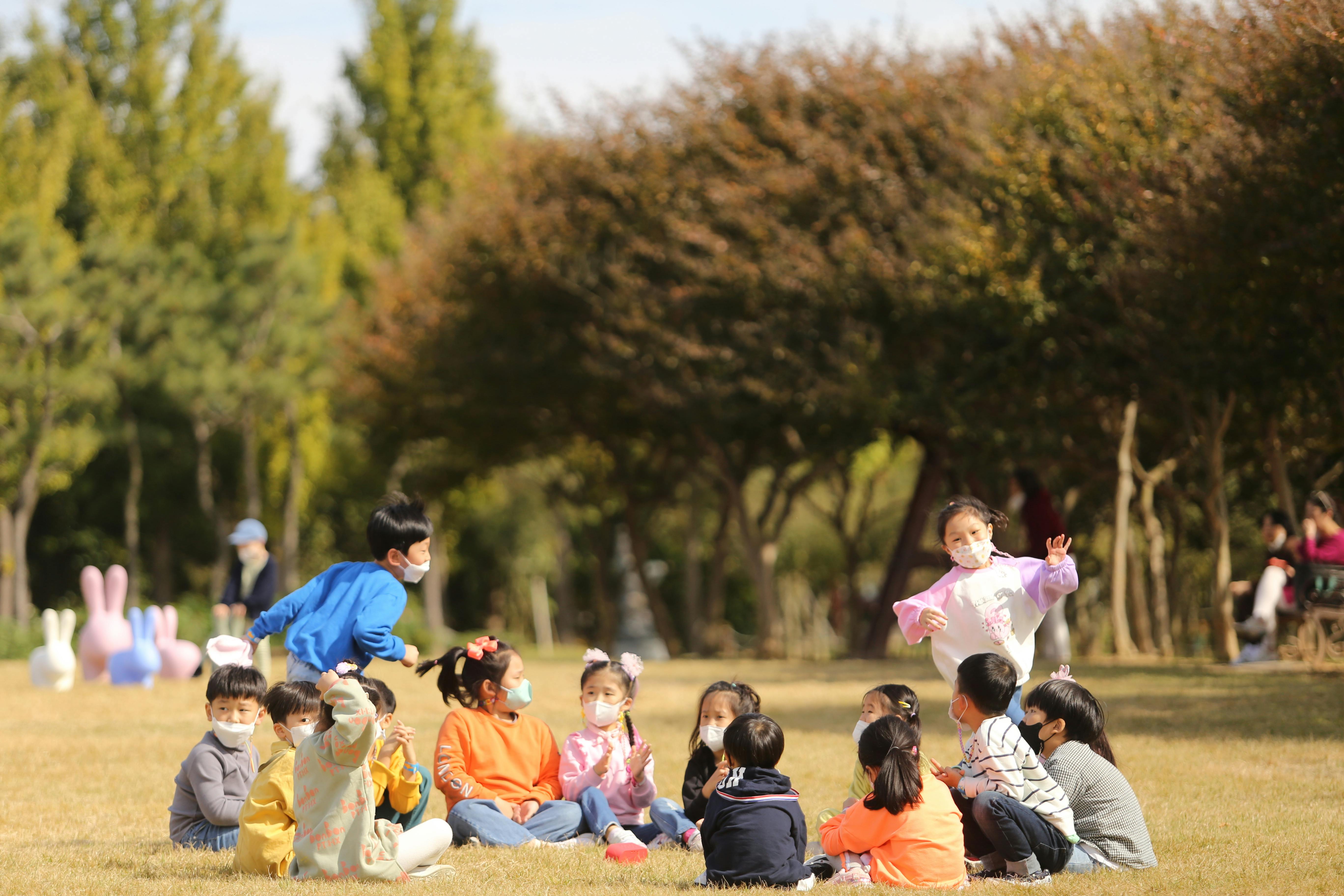 Group of children in masks playing outdoors in a sunny park setting.