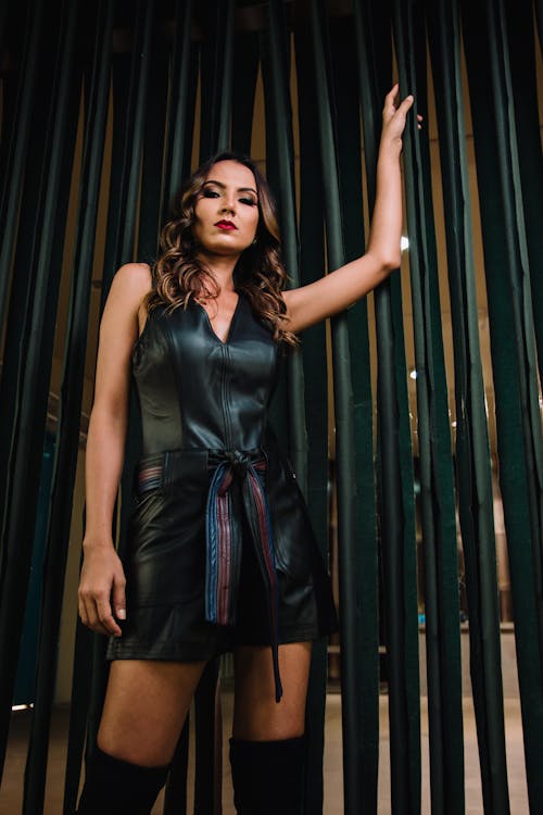 Woman in Black Sleeveless Dress in Front of Bamboo Wall