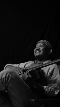 Monochrome portrait of a man with guitar expressing joy in relaxed pose.