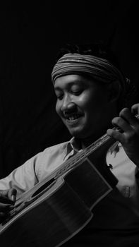Monochrome image of a smiling street musician playing an acoustic guitar in Indonesia.