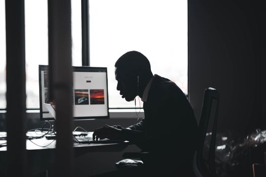 Silhouette of a man typing on a computer in an office setting during the day.
