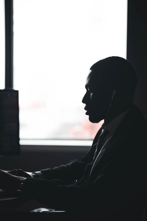 Free A silhouette of a man working at his desk next to a window, emphasizing focus and determination. Stock Photo