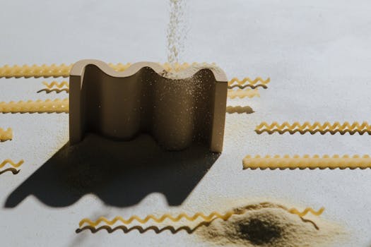 High-angle view of a pasta cutter with flour falling, capturing the art of food preparation.