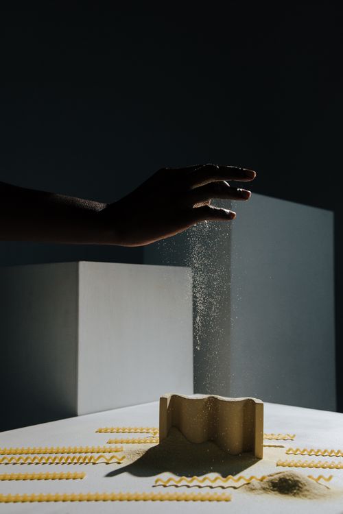 Free Artistic shot of a hand sprinkling flour over a pasta mold in a minimalist setting. Stock Photo