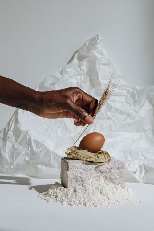 Free A creative arrangement of wheat, egg, and flour with a hand on a white background. Stock Photo