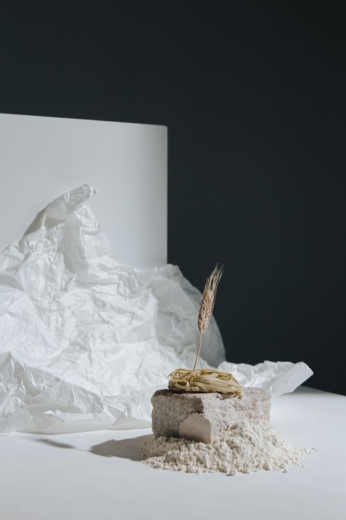 Free Artistic display of wheat, flour, and pasta on white surface with crumpled paper backdrop. Stock Photo