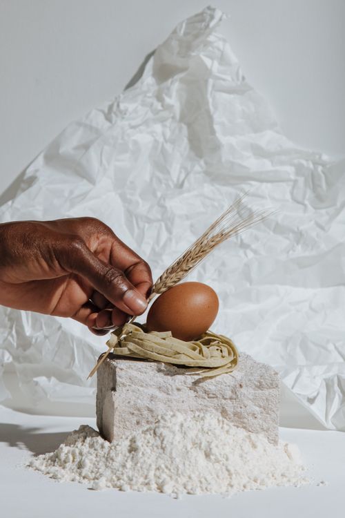 Free Artistic food arrangement featuring flour, egg, and hand on a white background. Stock Photo