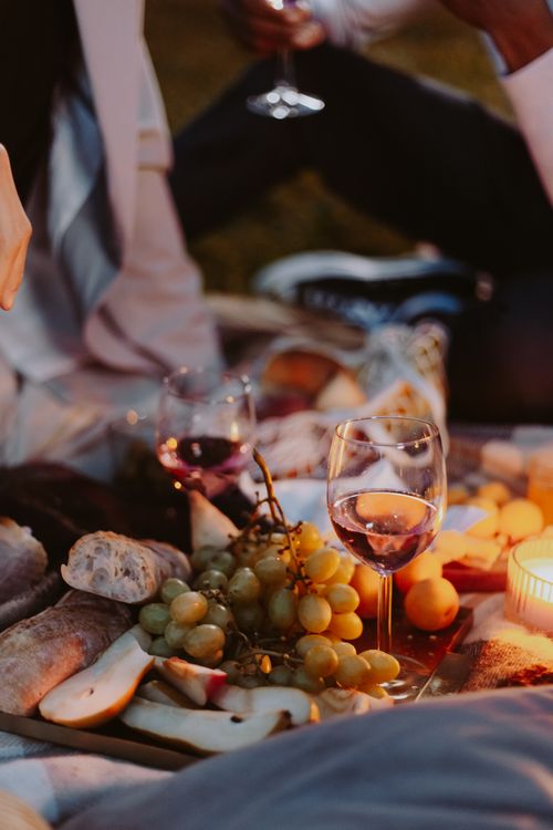 Free A warm evening picnic setup with wine, grapes, and candles on a blanket. Stock Photo