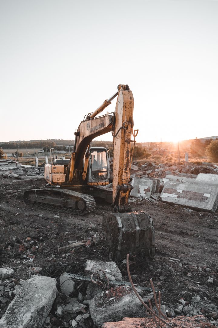 Excavator at a rubble-strewn site at sunset