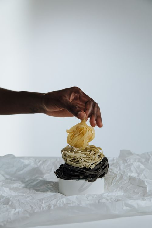 Free An artistic arrangement of colored pasta in a studio with a hand holding yellow noodles. Stock Photo