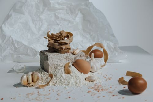 Free A creative still life featuring pasta, eggs, flour, and garlic with a rustic kitchen vibe. Stock Photo