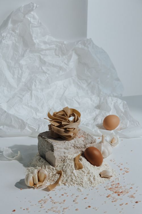 Free Artistic still life of pasta ingredients including eggs, flour, and garlic. Stock Photo