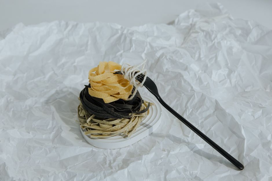 An artistic arrangement of colored pasta with a black fork on textured paper, showcasing food art.