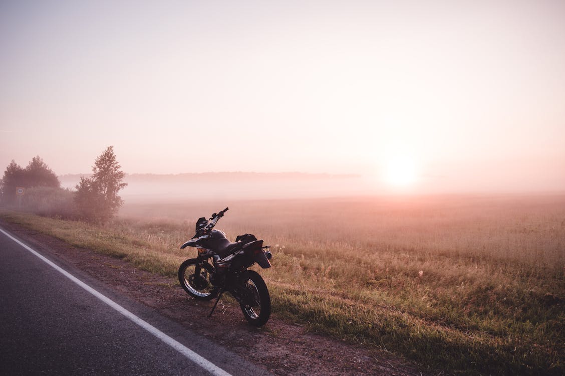 Motorcycle Parked on Side of the Road Near a Field at Sunrise
