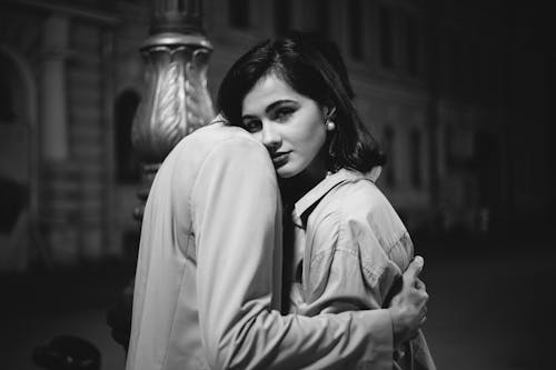 Free Monochrome Photo of a Woman Looking at the Camera while a Person is Hugging Her Stock Photo