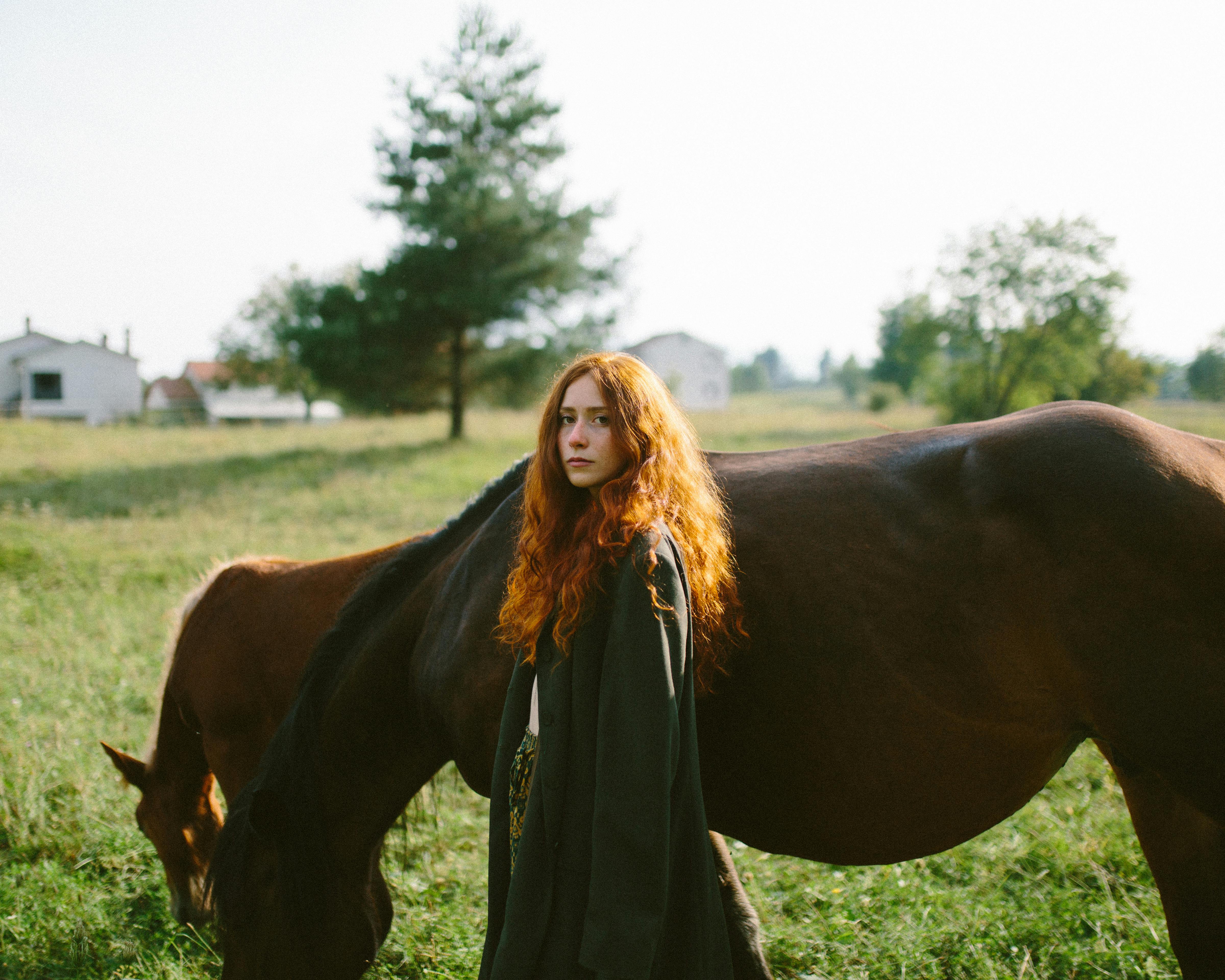 portrait of redhead woman standing against horses