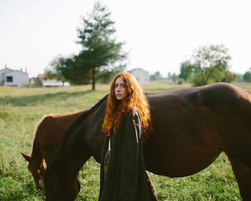 Portrait of Redhead Woman Standing Against Horses