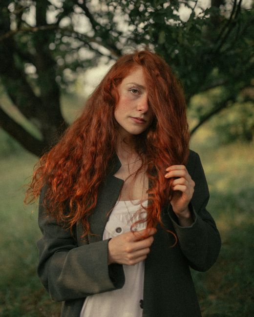 Artistic portrait of a red-haired woman in nature, showcasing her beauty and vibrant hair.