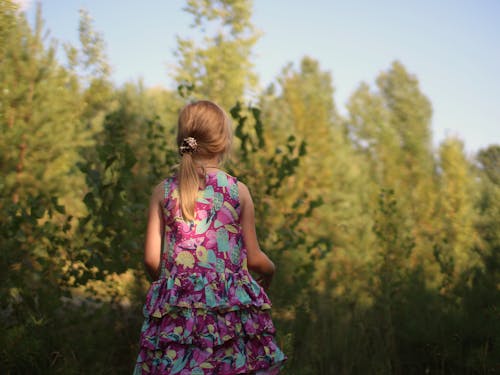 A Back View of a Woman in Printed Dress Standing Near the Green Trees