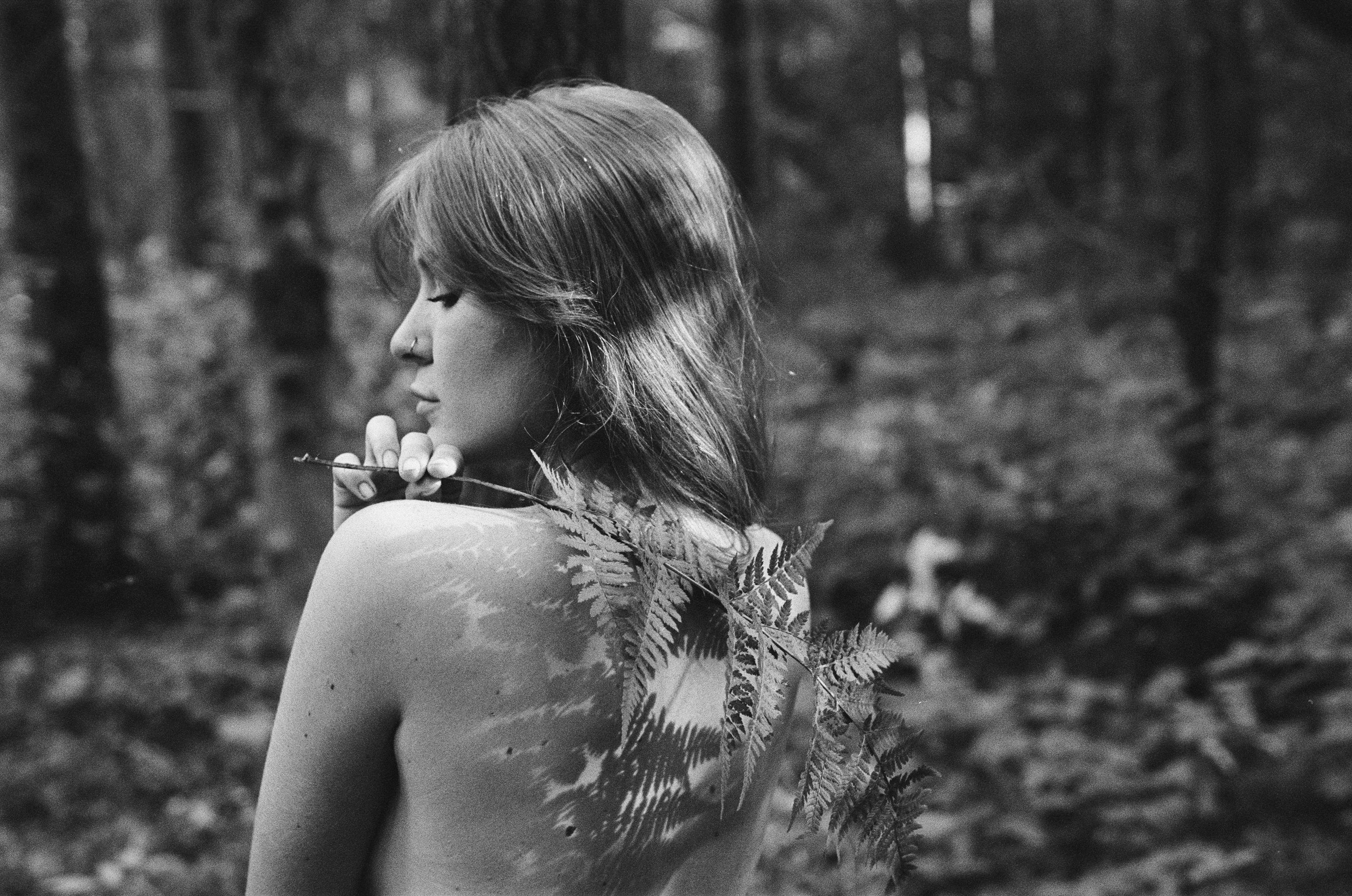 Elegant black and white portrait featuring a woman with a fern in a serene forest setting.