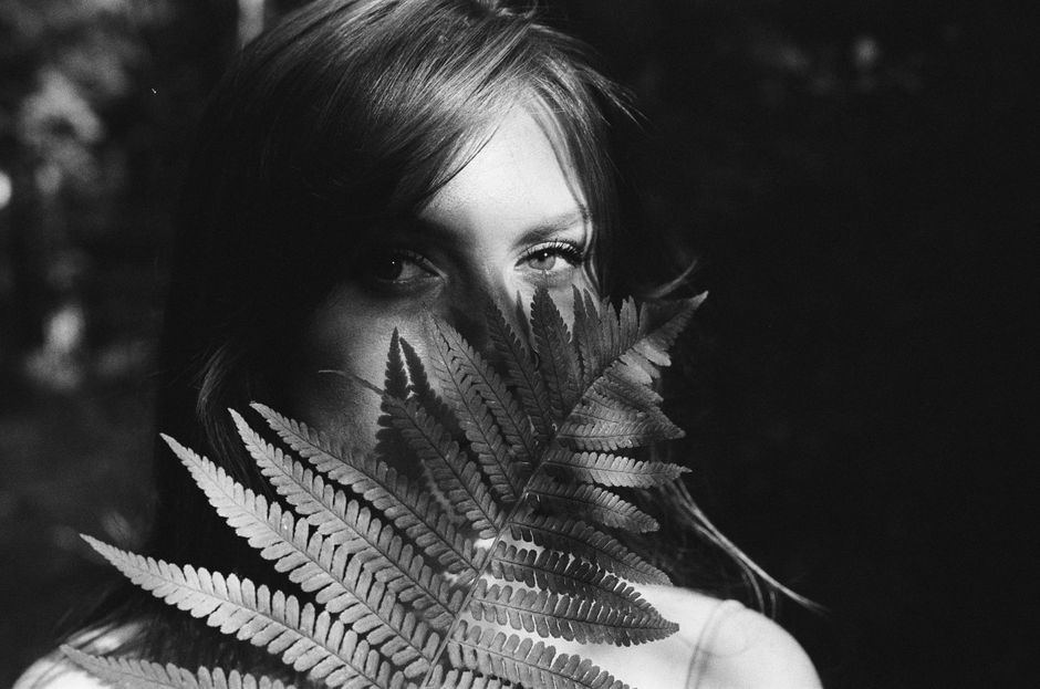 Black and white portrait of a woman partially hidden by fern leaves, creating a mysterious, artistic mood.